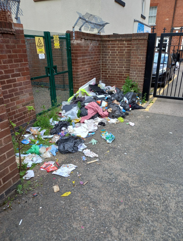 A lot of fly-tipped waste on the ground outside buildings