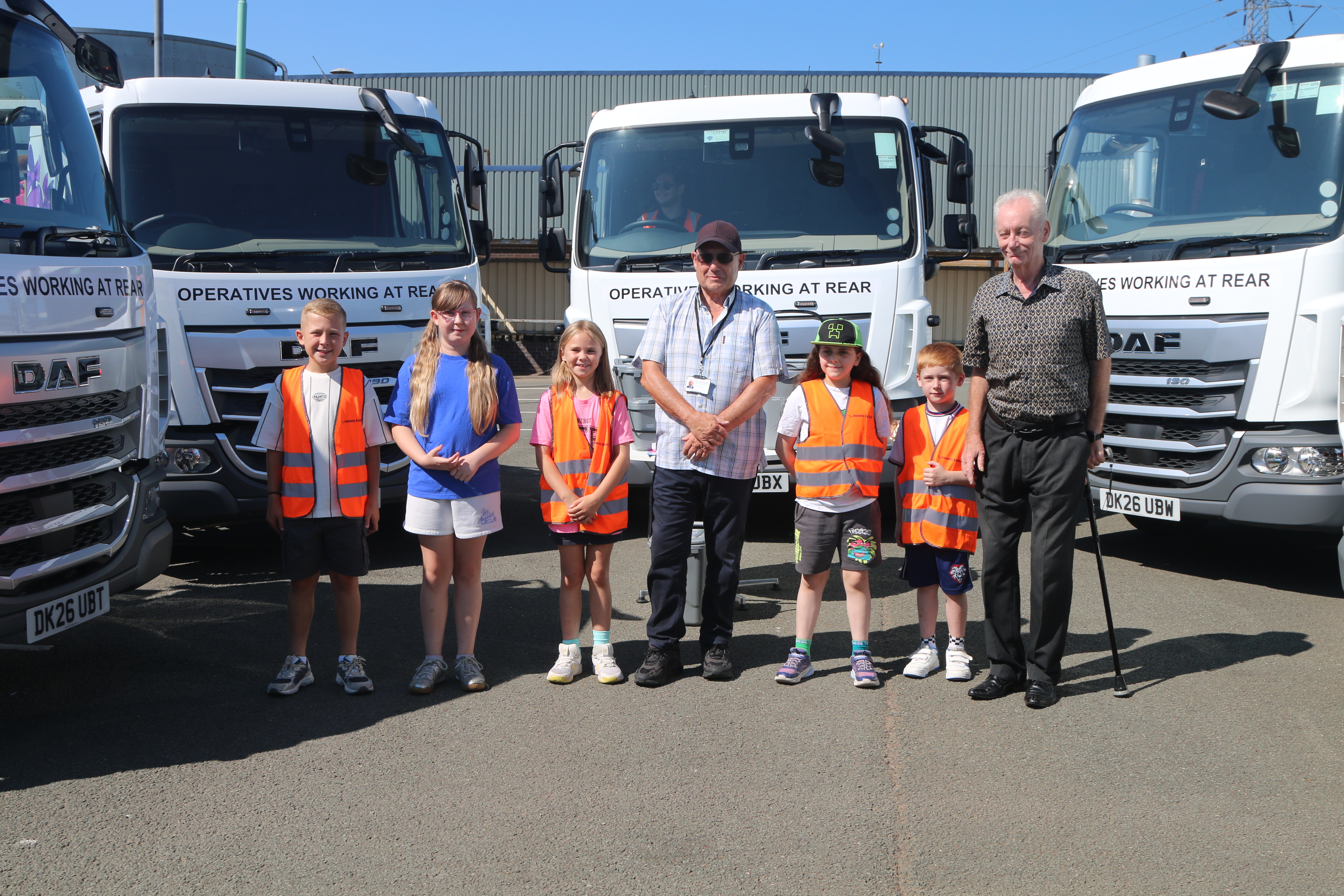 children standing by 3 white food waste trucks