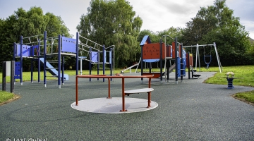 photo of playground equipment, including a blue climbing frame with a slide and a red climbing frame and swings