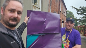 Two people holding up a purple sleeping bag shell