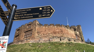 Tamworth Castle on a grassy hill. A signpost is in front of it.