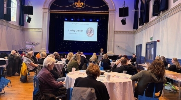 image of a room with a stage and screen and people sitting at round tables